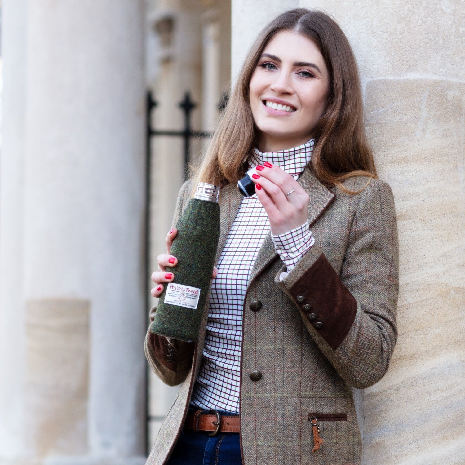Smiling woman in stylish outfit holding a 500ml Thermos Bottle with a Harris Tweed sleeve, showcasing the unique design of Thermos Bottles perfect for keeping drinks hot or cold.