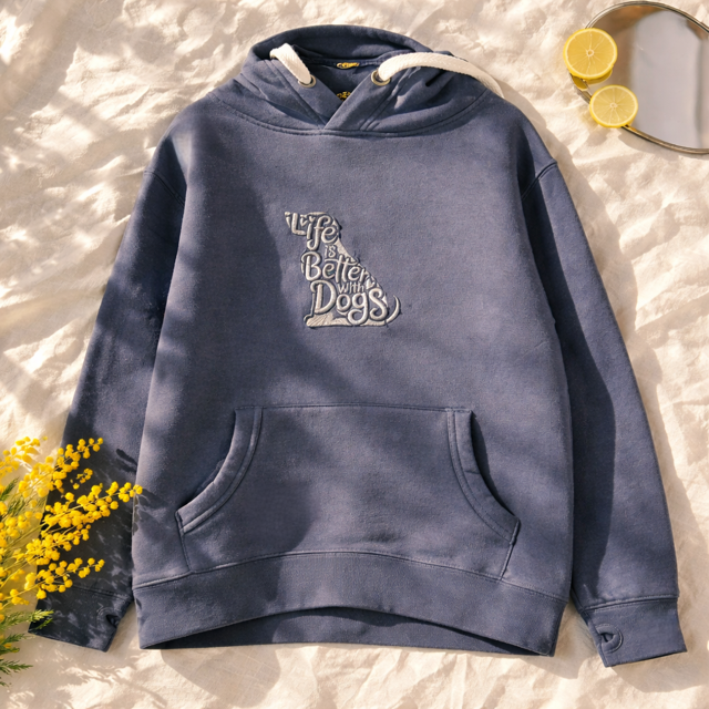 Blue hoodie with 'Life is better with dogs' text on a textured surface with flowers and lemons.